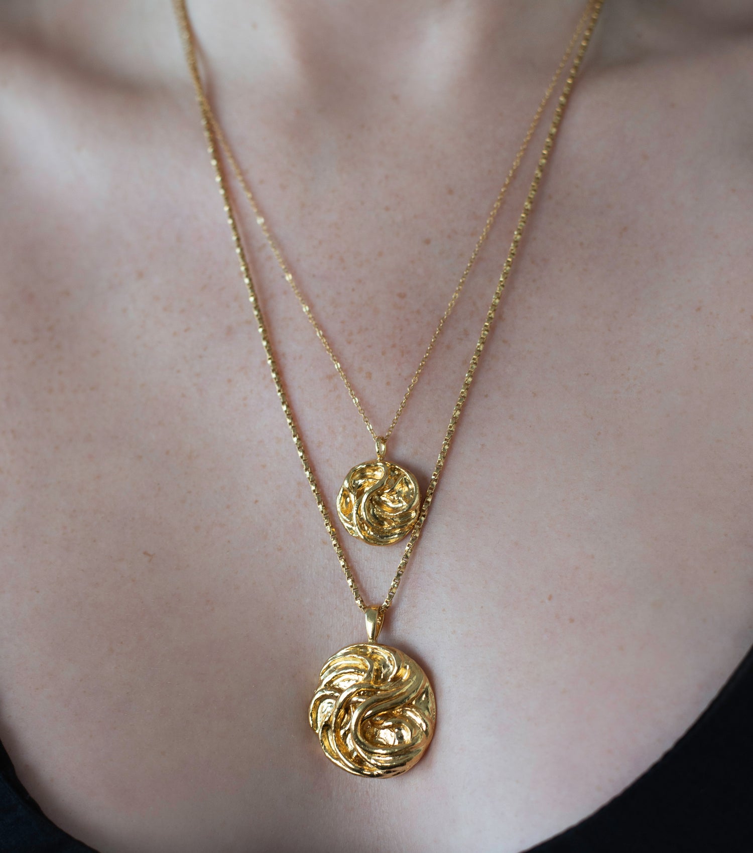 Close up of polished gold vermeil triskele necklaces with delicate golden chains