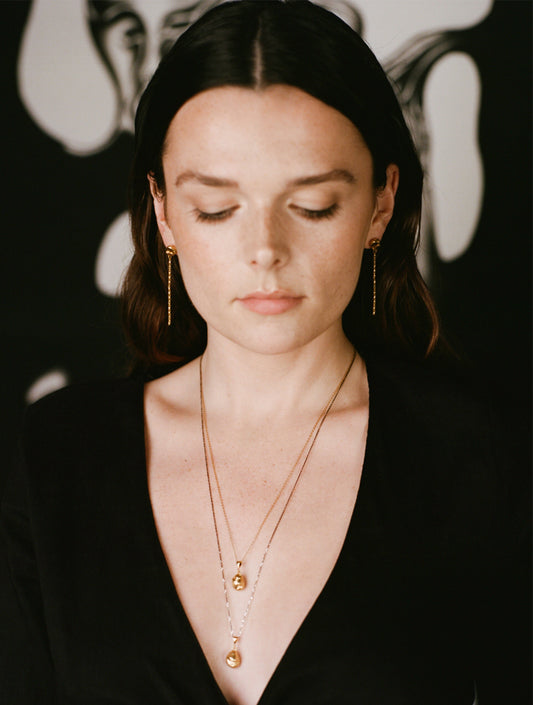Model wearing gold drop earrings layered with necklaces