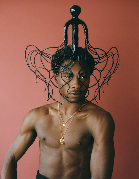 Model wearing black sculptural headpiece with two gold necklaces