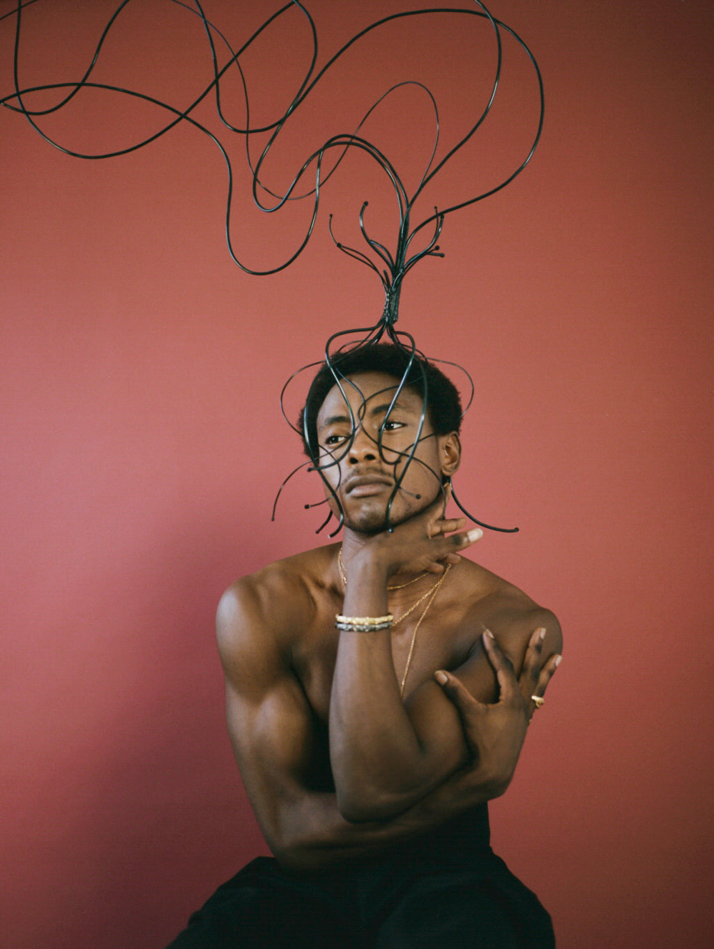 Model wearing large black headpiece, with red background and jewellery