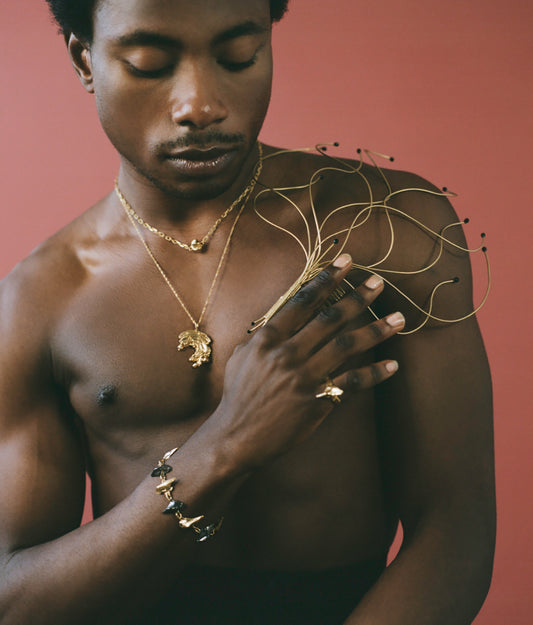 Model wearing gold layered chains and thick bracelets and a chunky ring