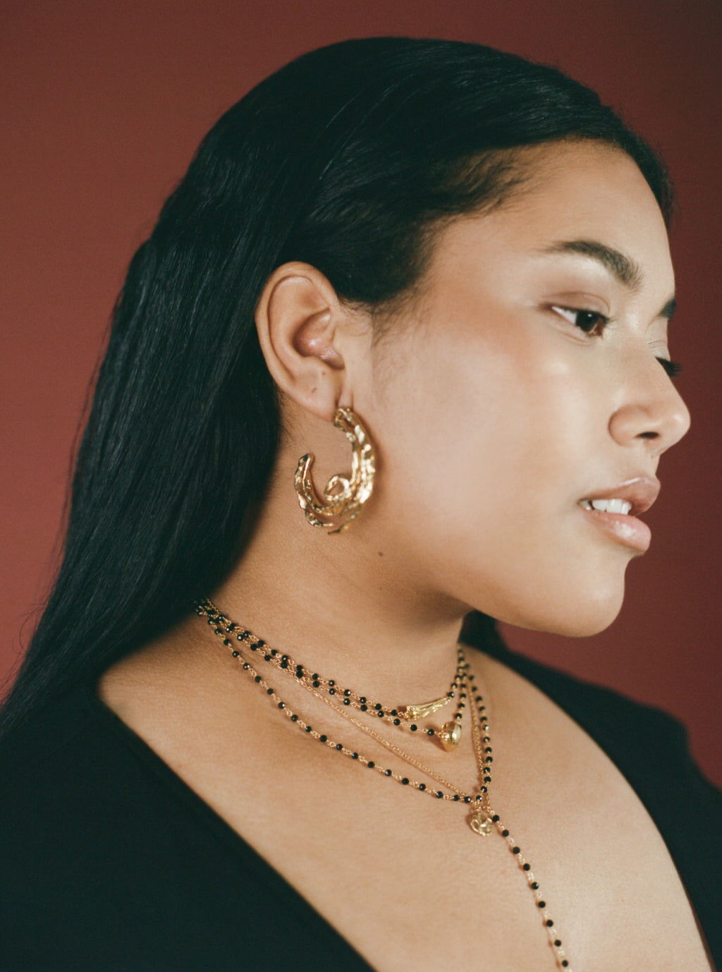Model wearing large gold hoops and black beaded chain necklaces
