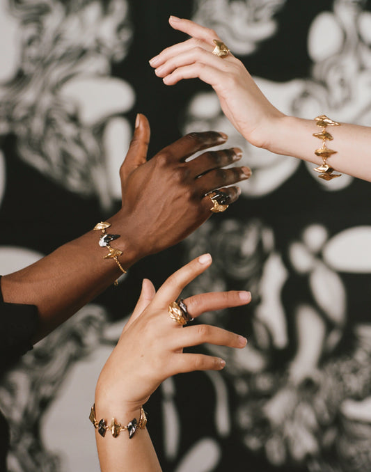 Model's hands wearing chunky rings and bracelets inspired by stone circles