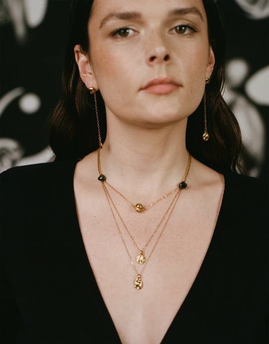 Model wearing layered necklaces and drop earrings
