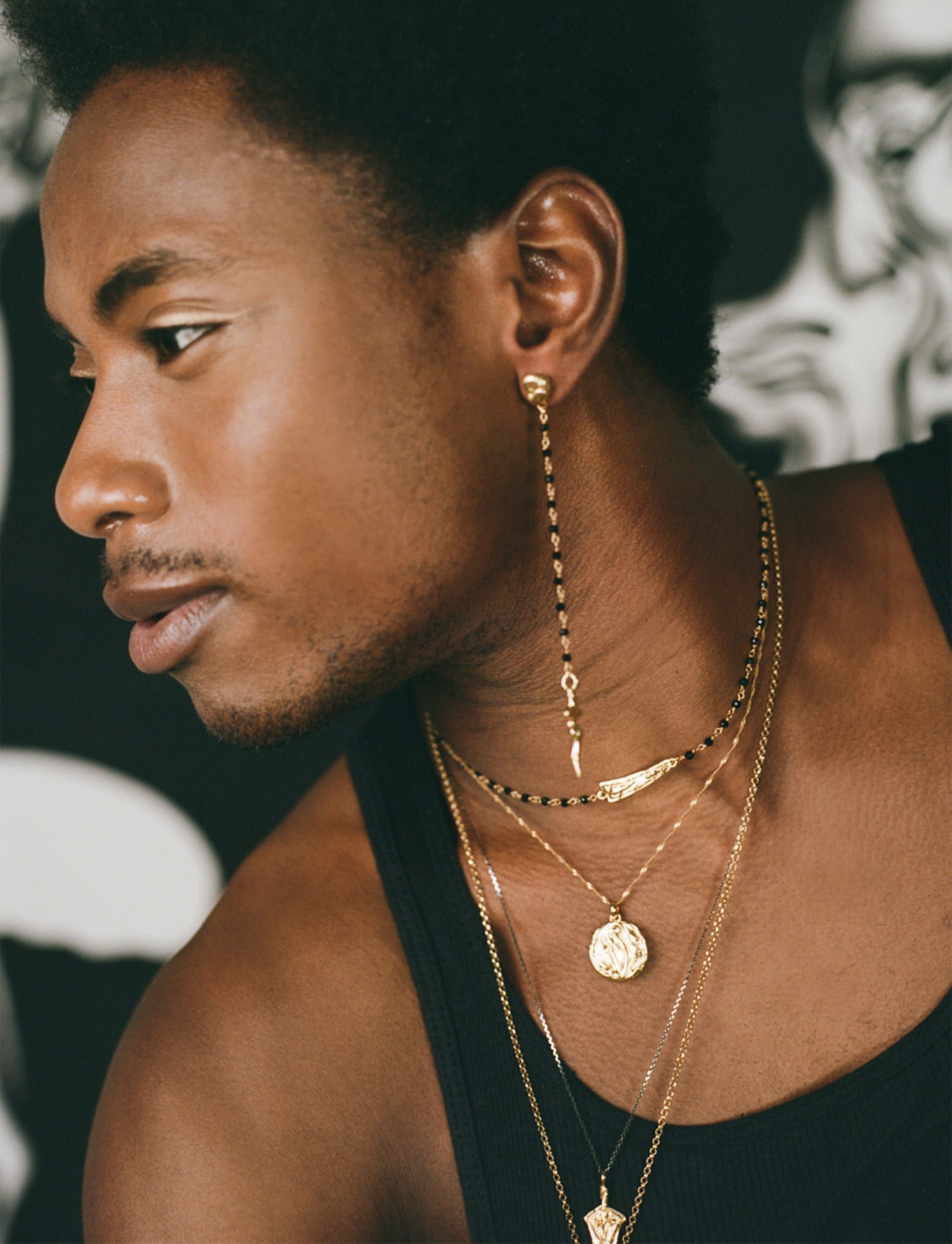 Model wearing rosary drop earring, with layered gold necklaces